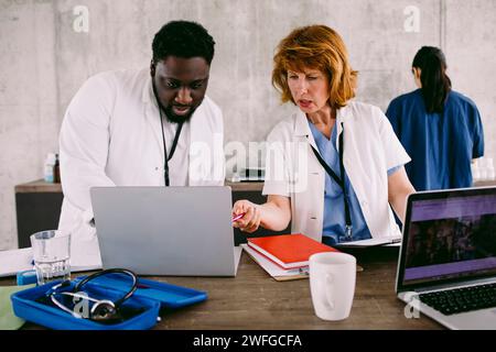 Colleghi medici che discutono su laptop alla scrivania in ospedale Foto Stock