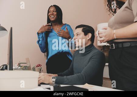 Imprenditore maschio sorridente seduto da colleghi femminili in ufficio Foto Stock