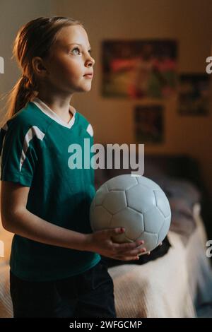 Ragazza elementare con la palla da calcio che sogna in camera da letto Foto Stock