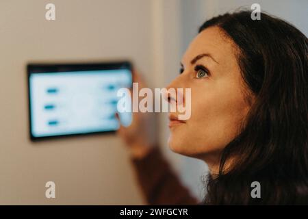 Donna matura che controlla la temperatura della stanza tramite un tablet digitale a casa Foto Stock
