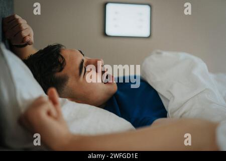 Ragazzo adolescente che sbadiglia sul letto mentre si sveglia la mattina a casa Foto Stock