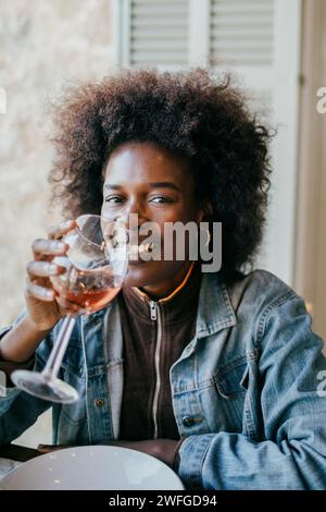 Ritratto di una giovane donna sorridente con acconciatura afro che beve vino nel patio Foto Stock
