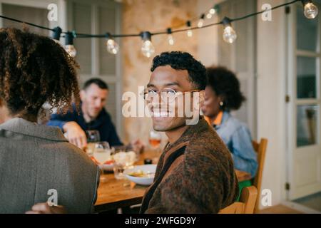 Ritratto di un giovane sorridente che indossa occhiali da vista seduto nel patio durante la cena Foto Stock