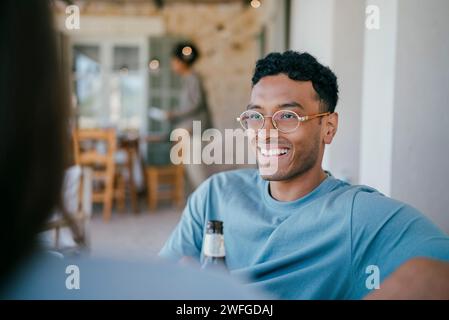 Un giovane uomo felice che parla con una donna seduta nel patio Foto Stock