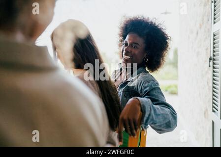 Donna felice con i capelli afro seduta da amici femminili nel patio Foto Stock