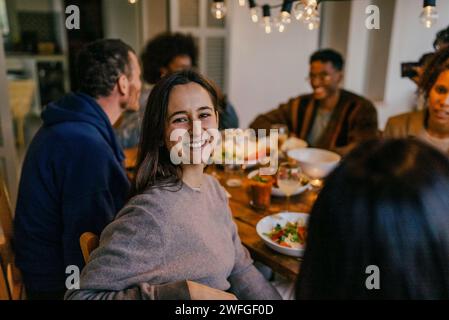 Ritratto di una giovane donna sorridente seduta con gli amici al tavolo da pranzo Foto Stock