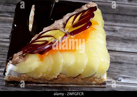 Torta di compleanno composta da due metà diversi pezzi, torta cremosa spugnosa per le celebrazioni, cioccolato fondente, caramello, panna alla vaniglia montata, fette di ananas Foto Stock