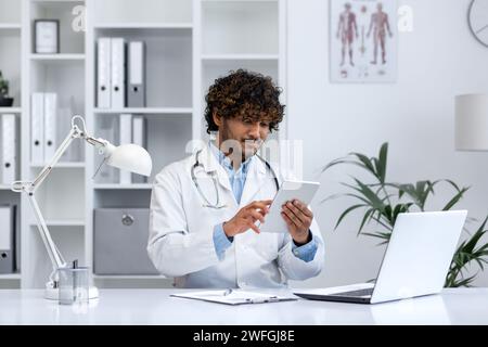 Giovane medico si è concentrato sulla tavoletta digitale mentre lavora in una clinica moderna. Rappresenta la tecnologia sanitaria. Foto Stock