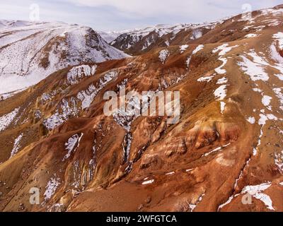 Riprese aeree che catturano le tonalità suggestive e le macchie innevate delle montagne Kyzyl-Chin simili a Marte nell'aspra regione russa dell'Altai. Foto Stock