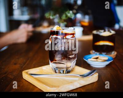 Americano Coconut ghiacciato. Un bicchierino trasparente di americano ghiacciato con acqua fresca di cocco e carne di cocco sul tavolo, una bevanda fredda estiva e una colazione casalinga Foto Stock