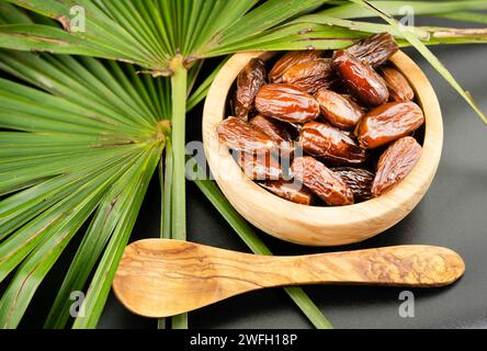 Datteri in una ciotola con foglia di palma e cucchiaio di legno Foto Stock