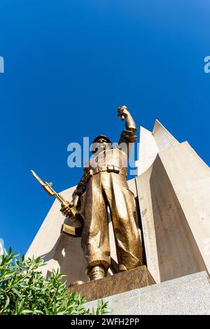 Vista dall'angolo basso di una statua di un soldato con una torcia e una pistola nel monumento Maqam Echahid contro un cielo blu. Foto Stock