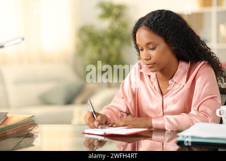 Freelance nero che scrive all'ordine del giorno seduto a casa Foto Stock