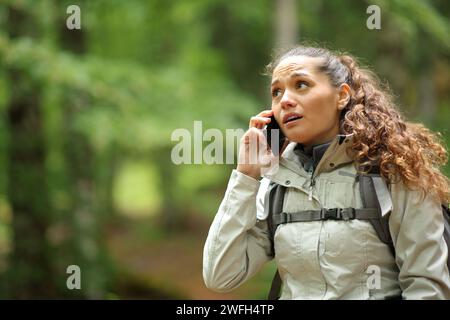 Preoccupato escursionista perduto che parla al telefono mentre cammina in una foresta Foto Stock