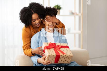 Una donna gioiosa copre gli occhi di un uomo da dietro, entrambi sorridenti con l'anticipazione Foto Stock