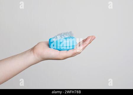 Mano con allineatori odontoiatrici invisibili trasparenti o supporti applicabili al trattamento ortodontico e contenitori blu. Foto Stock