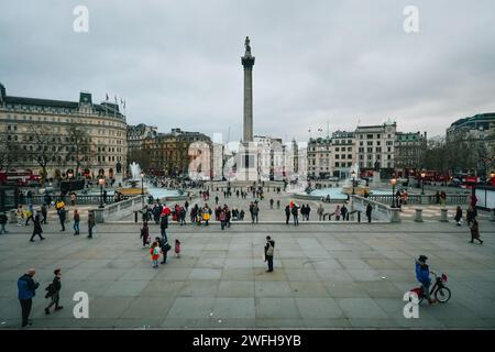 La folla passeggia attraverso la vasta Trafalgar Square mentre il sole tramonta Foto Stock