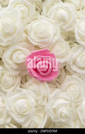 immagine verticale vista dall'alto dello sfondo di fiori bianchi e di un fiore rosa. fiori artificiali. Rose bianche artificiali e una rosa di foamiran. messa a fuoco morbida. posizione piatta Foto Stock