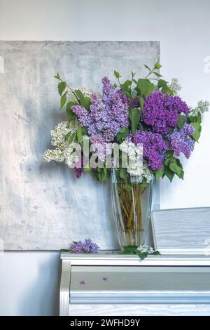 un bouquet di lillas in vaso trasparente su sfondo leggermente ruvido. immagine verticale di lilla, viola e fiori bianchi. tessera primavera o estate. messa a fuoco morbida Foto Stock