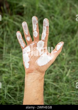 primo piano della mano dell'uomo ricoperta di vernice bianca sullo sfondo verde dell'erba. conservazione del concetto ambientale Foto Stock