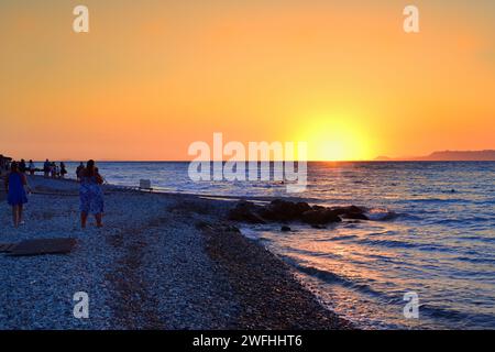 I turisti al tramonto sulla spiaggia di Ialyssos nell'isola greca di Rodi Foto Stock