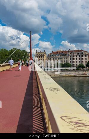 Lione, Francia, 2023. Persone che attraversano il ponte del Palais de Justice, con il Presqu'île (2° arrondissement) sullo sfondo (verticale) Foto Stock