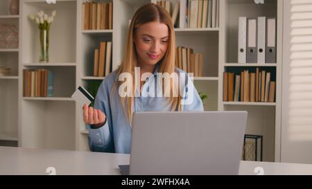 Donna caucasica felice a casa ufficio con laptop shopping online donna d'affari sorridente paga l'acquisto in Internet con il computer e la ragazza della carta di credito della banca Foto Stock