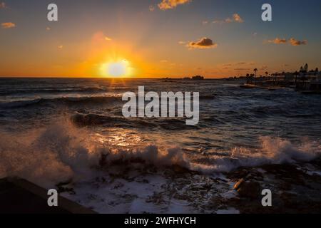 Splendido tramonto sul mare mediterraneo tempestoso, Paphos, Cipro. Spiaggia rocciosa, inverno, nuvole di tempesta nel cielo. Foto Stock