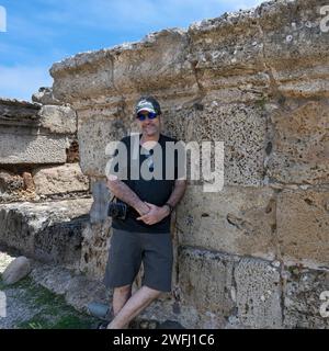 Turista maschio addossato a un muro di pietra presso l'antica città pre-romana di Nora su una penisola nei pressi di Pola, Sardegna, Italia Foto Stock