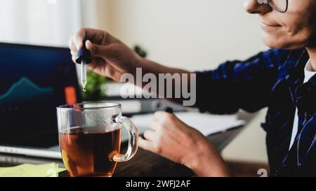 Olio di CBD. Donna d'affari che prende cannabis goccia nella bevanda da tè per il trattamento dell'ansia e dello stress. Medicina alternativa Foto Stock