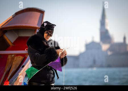 Venezia, Veneto, Italia - 28 gennaio 2024: Maschera donna in costume di Carnevale che aiuta con le decorazioni sui partecipanti barche del Carnevale veneziano apertura R. Foto Stock