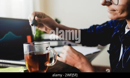 Olio di CBD. Donna d'affari che prende cannabis goccia nella bevanda da tè per il trattamento dell'ansia e dello stress. Medicina alternativa Foto Stock