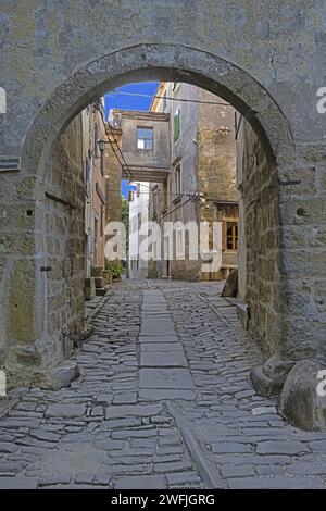 Ammira attraverso un'entrata ad arco lungo una strada acciottolata in un antico villaggio senza persone durante il giorno Foto Stock