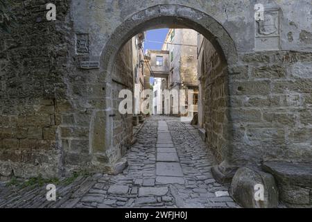 Ammira attraverso un'entrata ad arco lungo una strada acciottolata in un antico villaggio senza persone durante il giorno Foto Stock