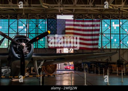 Un aereo d'epoca della seconda Guerra Mondiale parcheggiato all'interno di un appendiabiti con una bandiera degli Stati Uniti sullo sfondo - Pearl Harbor, Hawaii Foto Stock