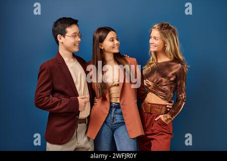 adorabili, allegri e variegati adolescenti in abiti eleganti e vivaci che si divertono su sfondo blu, giorno dell'amicizia Foto Stock