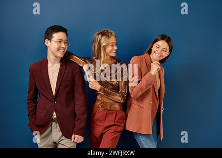 allegramente eleganti e variegati adolescenti in abiti alla moda sorridenti felicemente su sfondo blu, giorno dell'amicizia Foto Stock