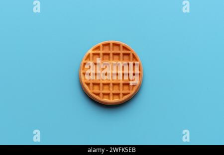 Vista dall'alto con un singolo waffle belga rotondo minimalista su un tavolo di colore blu. Foto Stock