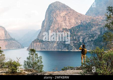 Uomo con uno zaino che scatta foto di una splendida vista del serbatoio di Hetch Hetchy Foto Stock