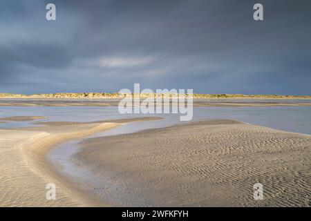 Mentre le nuvole di tempesta si accumulano sopra le dune, la splendida spiaggia di West Wittering è illuminata dal sole che rivela sabbia scolpita durante la bassa marea. Foto Stock