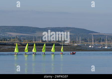 I giovani sulle loro dingie a vela vengono trainati da una COSTOLA con la bassa marea nel porto di Chichester con ampie vedute delle South Downs Foto Stock