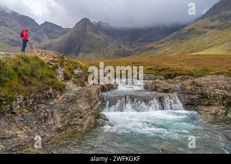 Un visitatore e un cane terrier di confine in una delle numerose cascate delle Fairy Pools, Black Cuillin Mountains, Isle of Skye Foto Stock