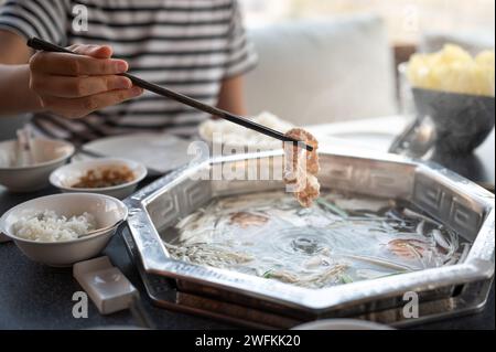 Donna che immerge carne cruda per cucinare in una zuppa bollente a forma di hot pot. Questo piatto tradizionale asiatico è preparato con molti ingredienti e carne Foto Stock