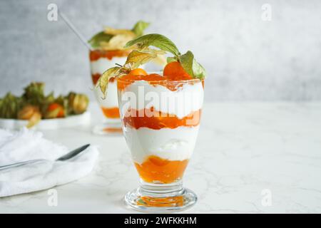 Due bicchieri di dessert stratificato con yogurt proteico e frutta fisalis Foto Stock