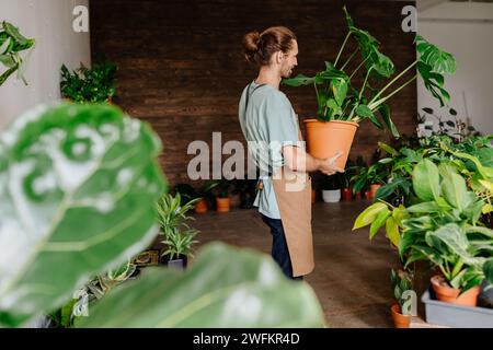 Uomo impegnato in uniforme che lavora in un negozio di fiori presso la sua boutique floreale. Bell'uomo che tiene un vaso di fiori. Il business floristico e il concetto di persone. Foto Stock