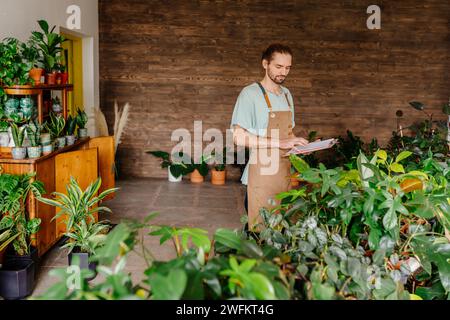 Ritratto di un fioraio africano di successo che ripiantava fiori in un negozio di fioristi usando il terreno che indossava il grembiule. L'uomo fiorista mette le piante in scrivania al fiore Foto Stock