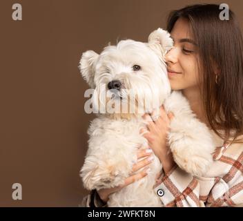 Ritratto di una ragazza con un cane bianco del West Highland White Terrier su sfondo marrone Foto Stock