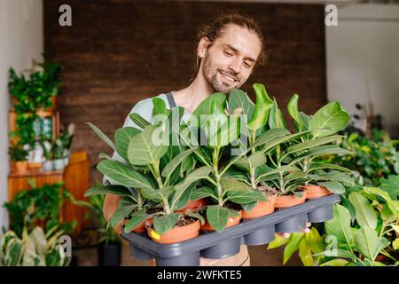 Un ritratto di un giovane uomo caucasico giardiniere che indossa un grembiule al chiuso al negozio di piante, piantando fiori. Foto Stock