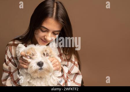 Ritratto di una ragazza con un cane bianco del West Highland White Terrier su sfondo marrone Foto Stock