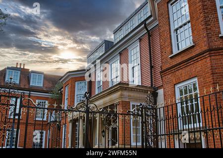 Elegante edificio in mattoni con grandi finestre dietro porte di ferro ornate sotto un suggestivo cielo al tramonto. Foto Stock